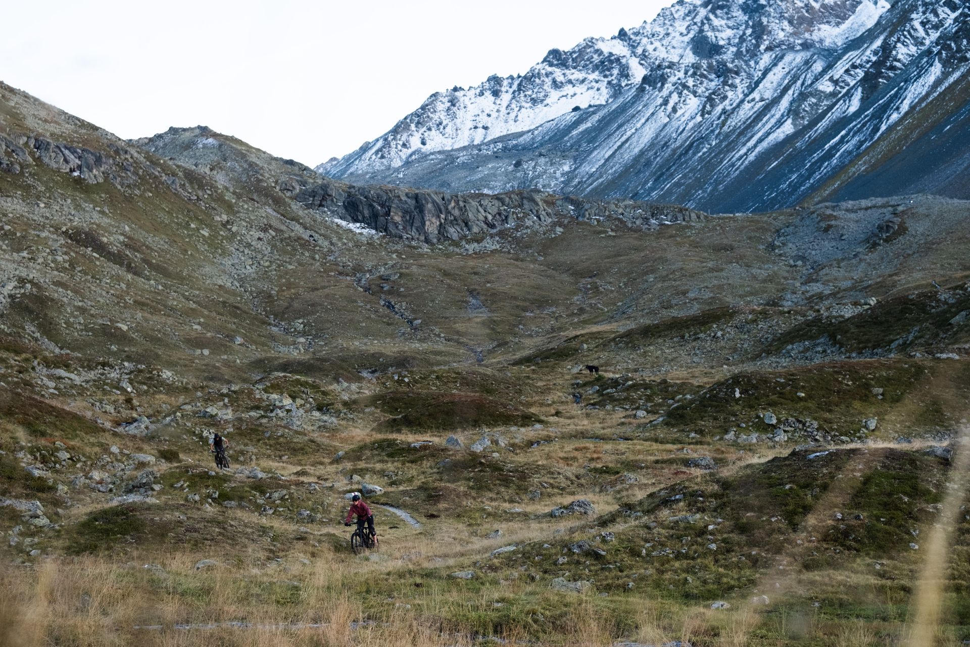 Riders crossing a remote alpine valley below snow-covered peaks