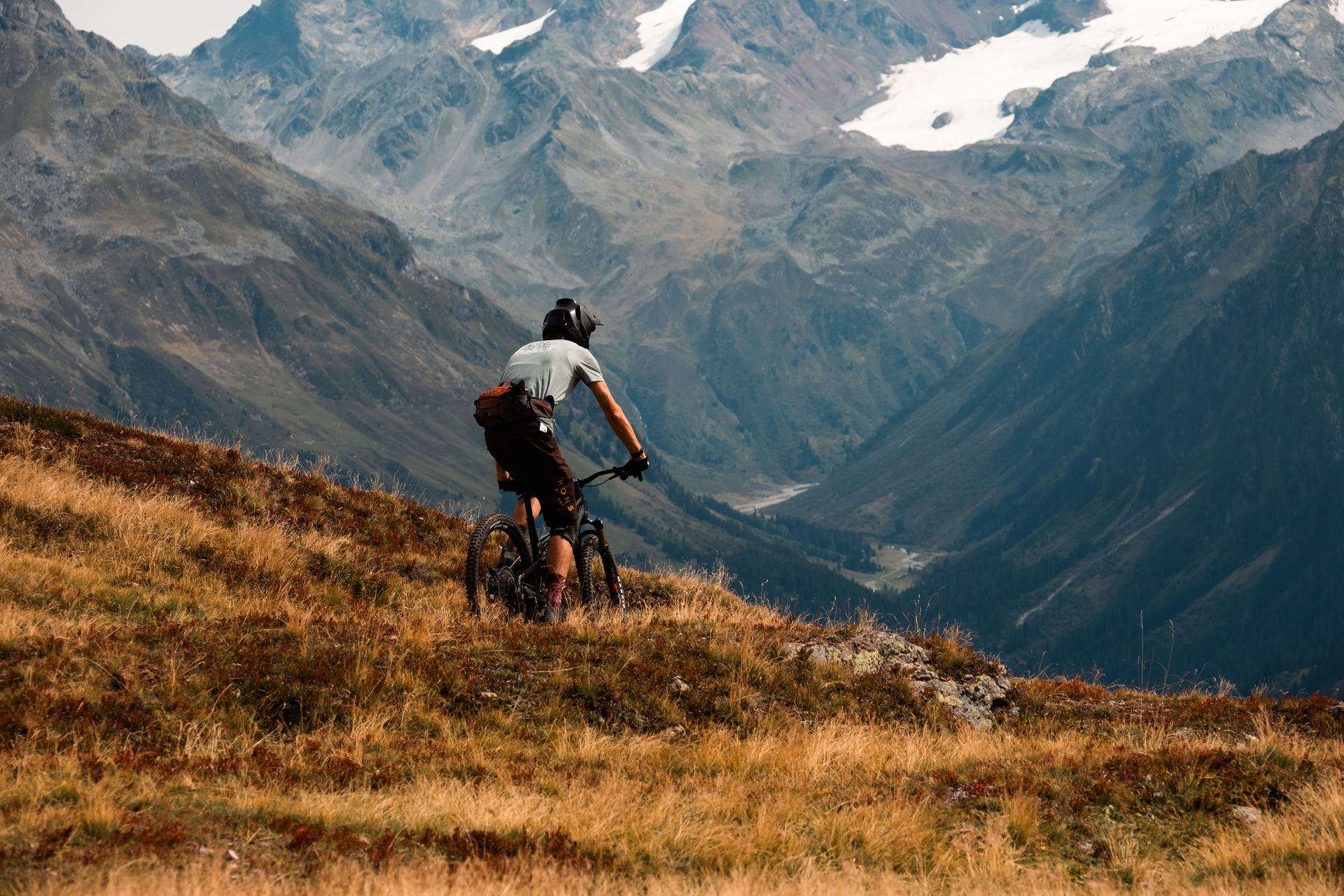 Rider descending a remote grassy ridge toward a valley