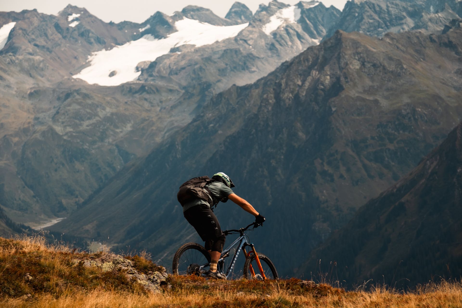 Rider descending a ridgeline above the Klosters valley, snow-capped peaks behind