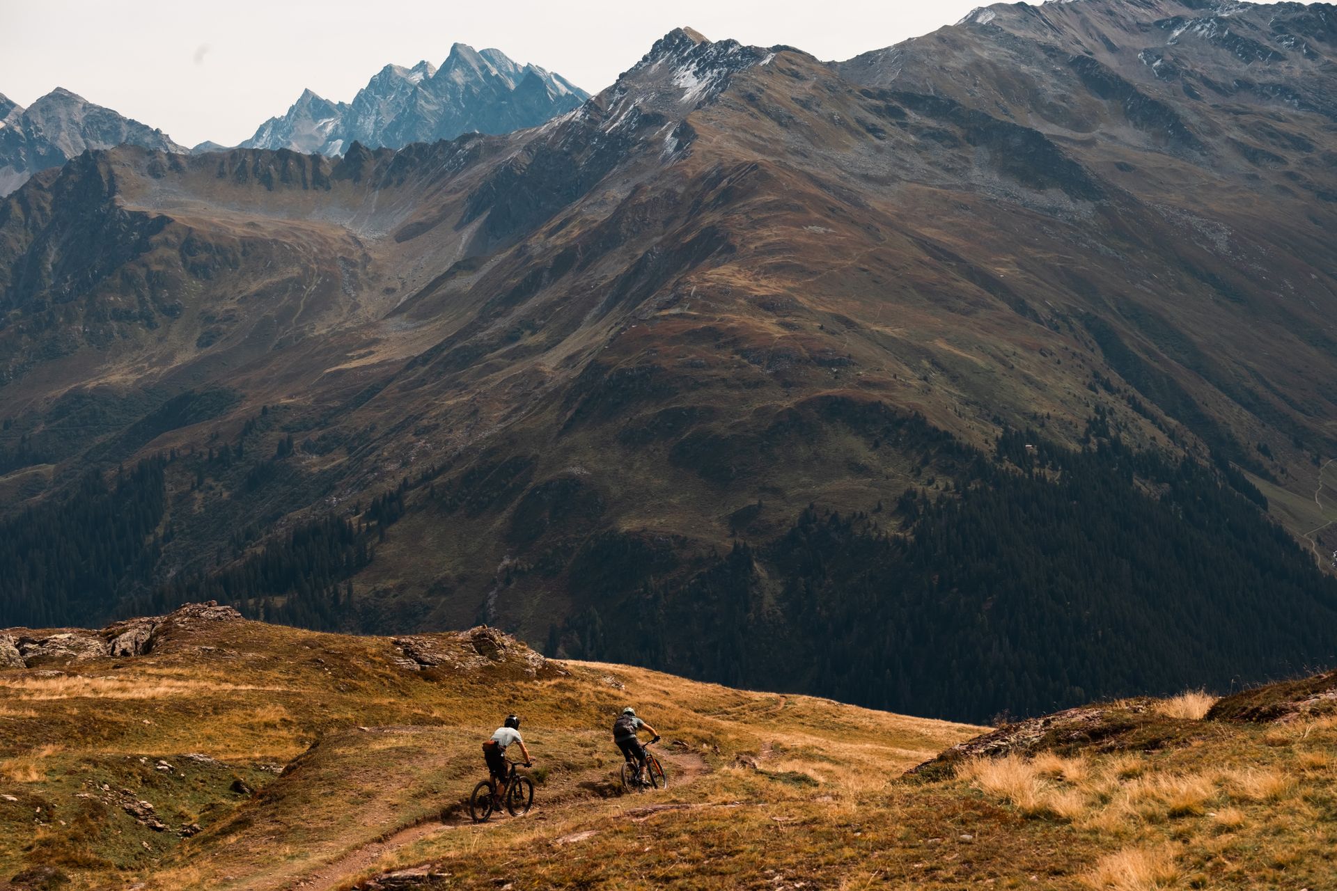 Two riders on a ridge trail with dramatic mountain backdrop