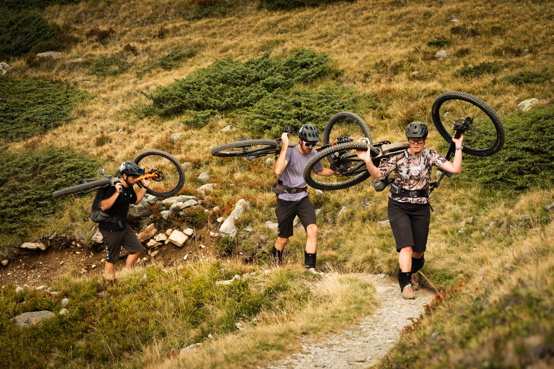 Group carrying bikes across a grassy slope