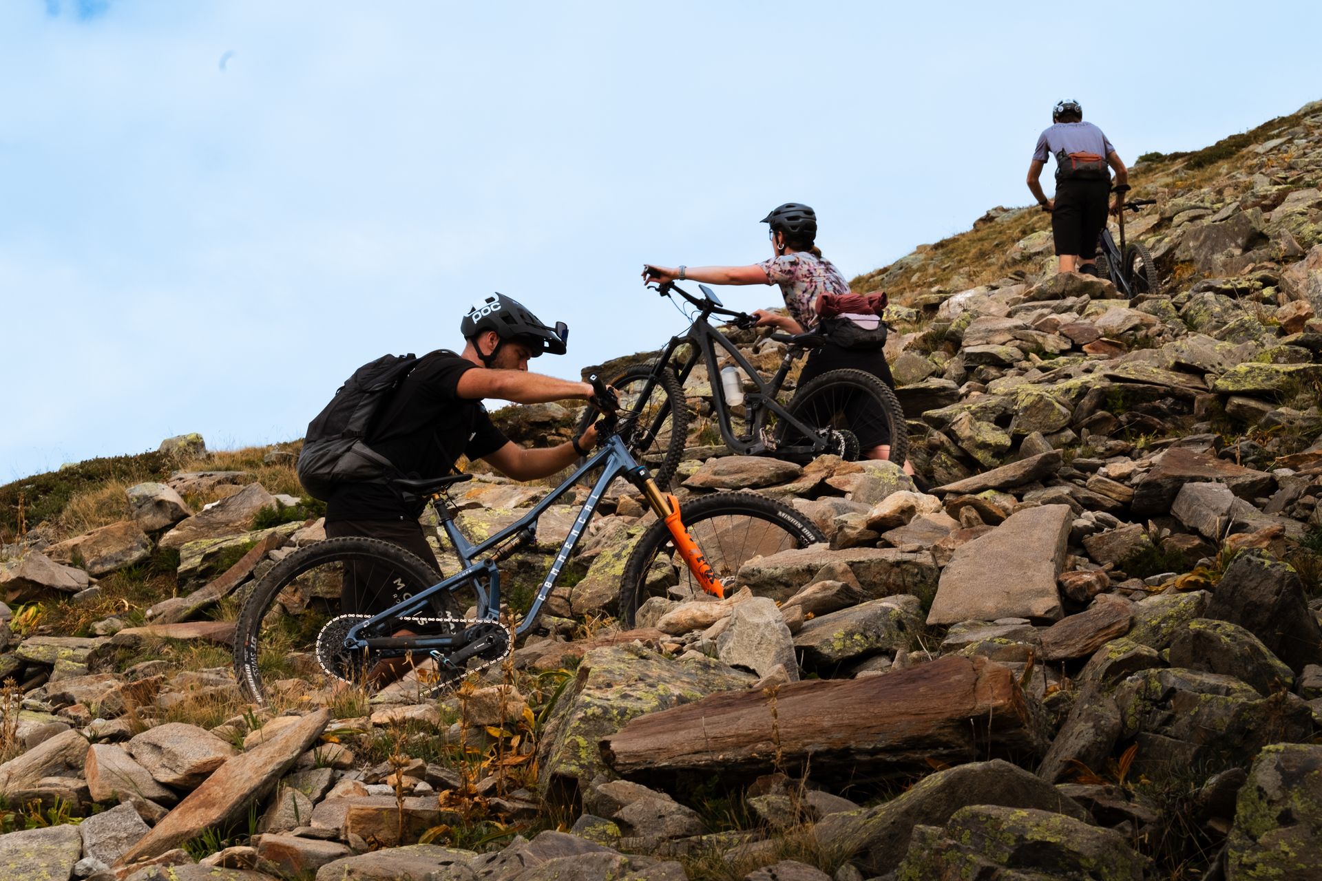 Riders pushing bikes across a rocky ridge